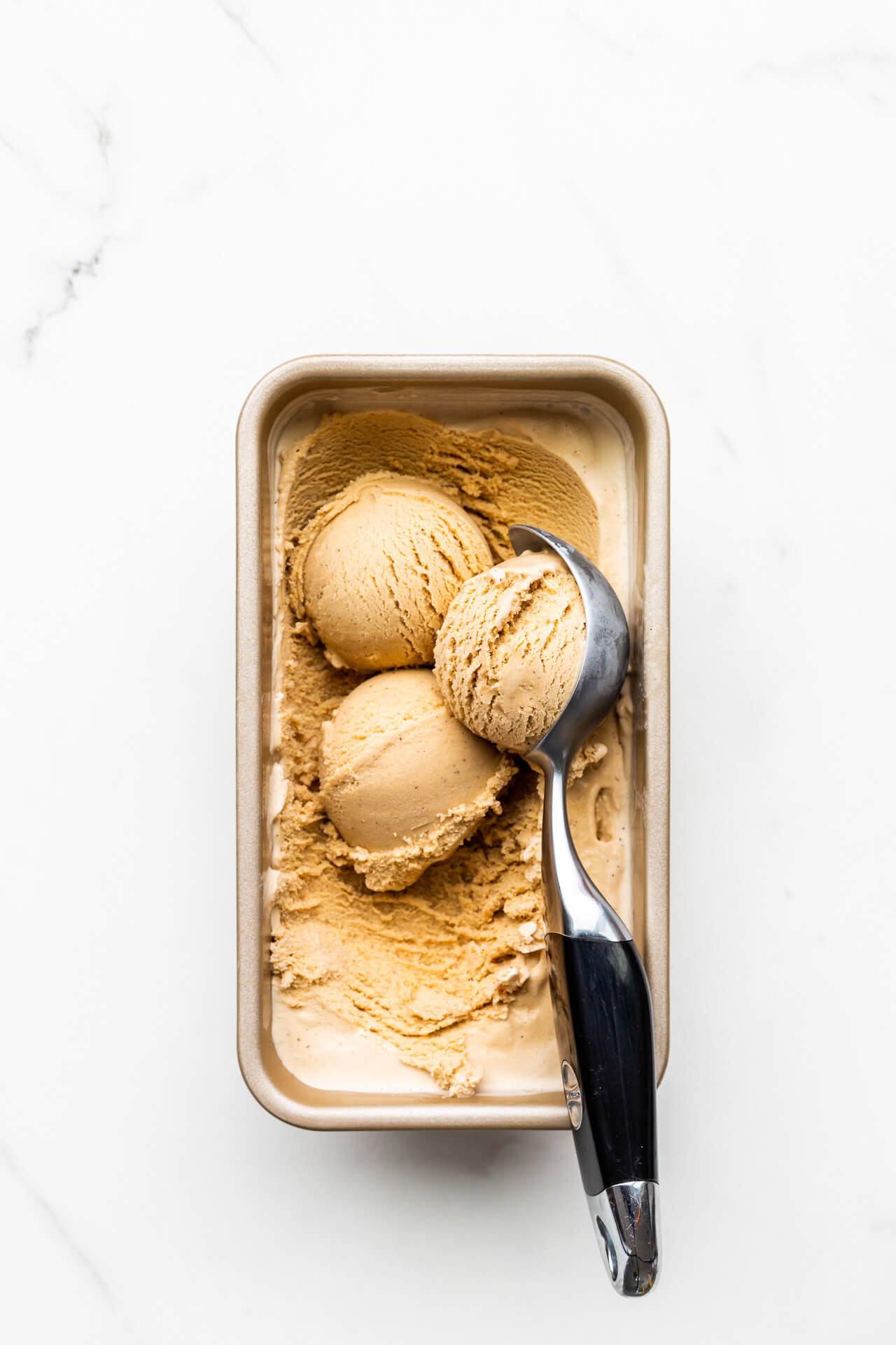 Scooping homemade black tea infused ice cream frozen in a loaf pan with a black handled ice cream scoop