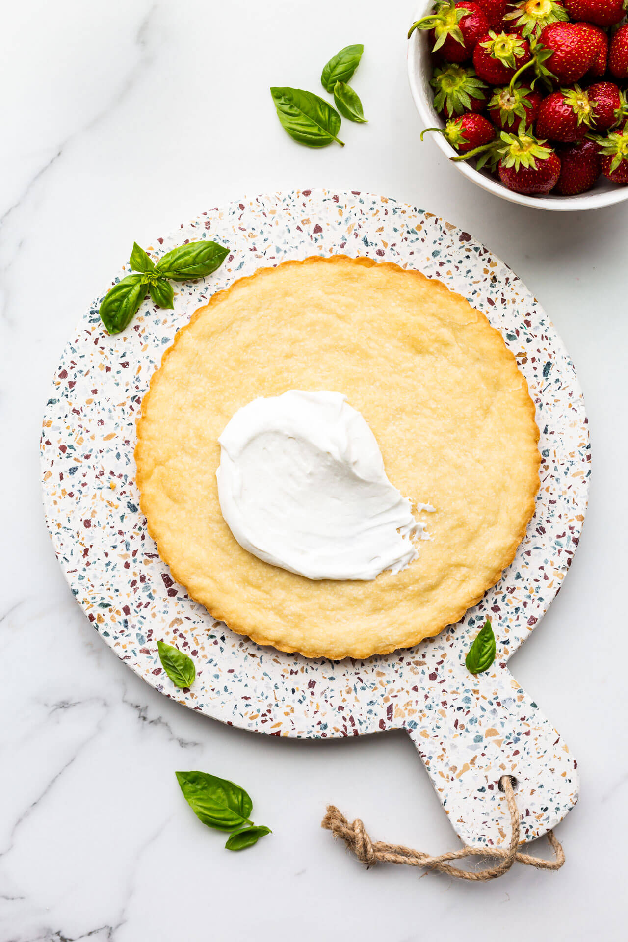 Assembling a strawberry tart, first topping with yogurt whipped cream and then fresh strawberries, and garnishing with fresh basil leaves