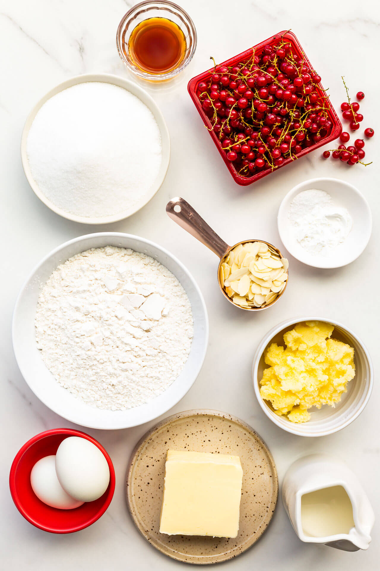 Ingredients measured out in small bowls and plates to make red currant muffins from scratch with a sugary crisp topping and sliced almonds