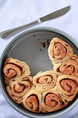 Unglazed cinnamon raisin buns in round cake pan with knife