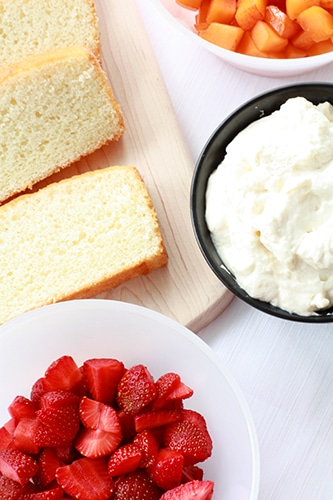 Components for assembling a trifle: sliced sponge cake, sliced strawberries, whipped cream, and chopped apricots