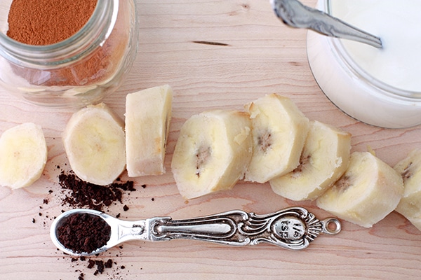 Ingredients for coffee banana smoothie made with coffee grinds, frozen banana, cinnamon, and milk.