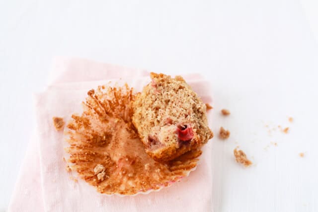 Half of a strawberry rhubarb muffins with crumble topping on a paper liner with a pink napkin