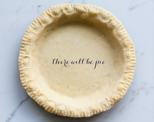 Unbaked pie crust lining pan with floral imprint on edges on marble surface