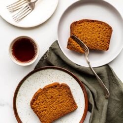Slices of pumpkin bread served on speckled plates with a cup of tea and green linen