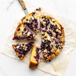 Sliced black currant cake on parchment paper with a wood-handled knife to serve