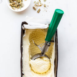 Scooping homemade cardamom ice cream with a disher. Small bowl of cardamom pods nearby