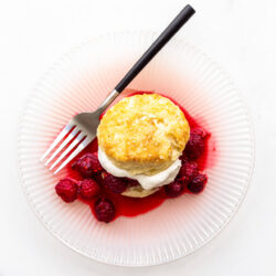 A raspberry shortcake with homemade biscuit, whipped cream, and berries on a pink plate with a fork with black matte handle